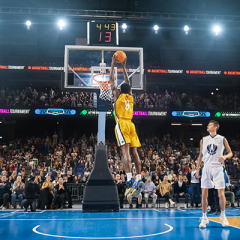 Professional basketball game. Focal point is one player in air about to do a slam dunk.