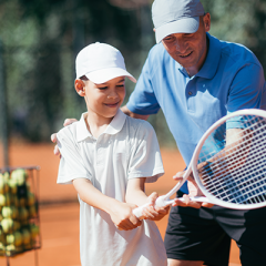 Coach guiding young boy with tennis racquet