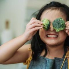 girl playing with broccoli covering her eyes 
