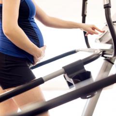 close up on belly of a pregnant lady on an elliptical machine