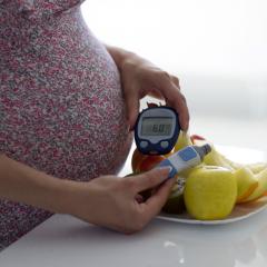 pregnant woman monitoring blood sugar in front of bowl of fruits